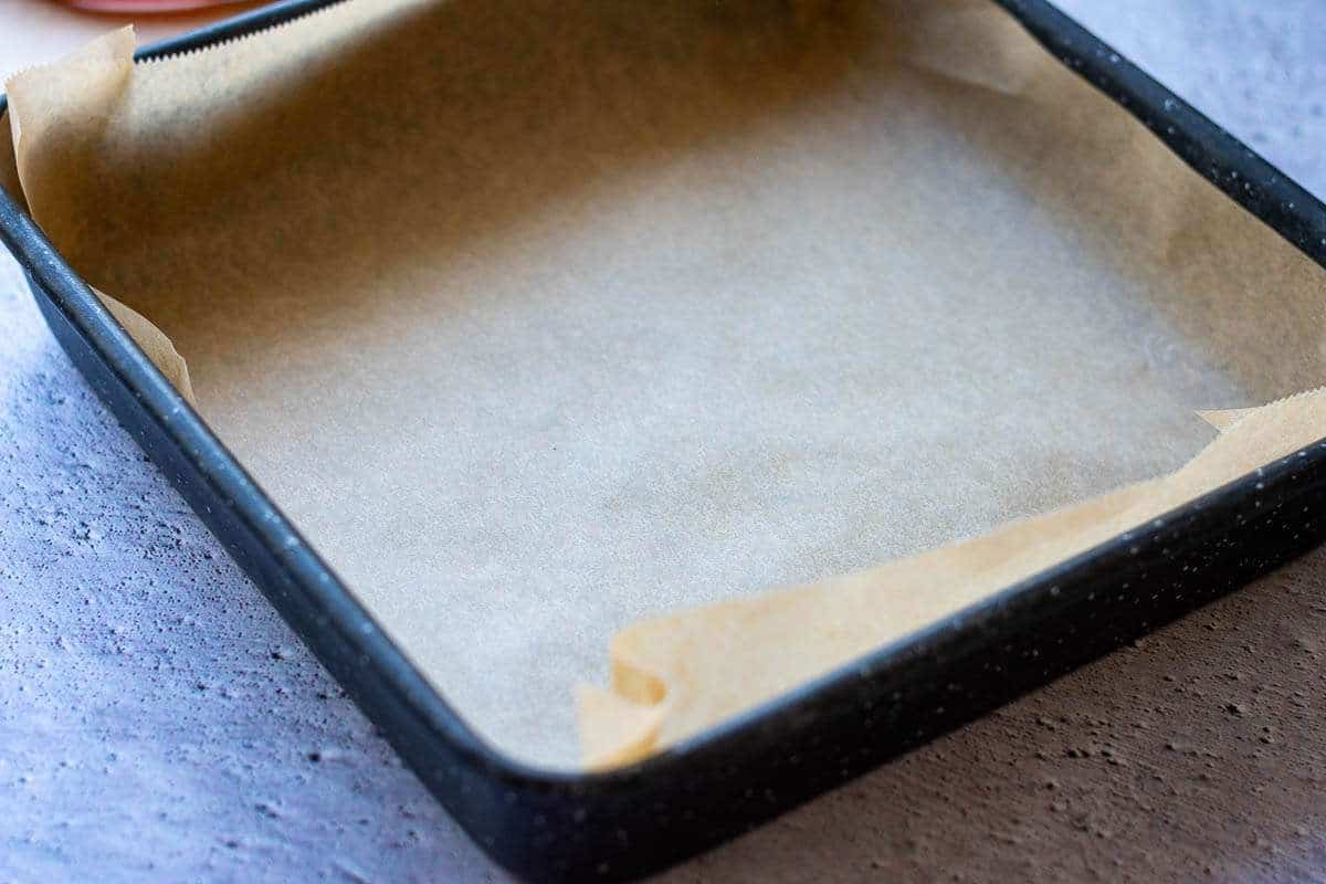 A square baking tray with high rims lined with parchment paper.