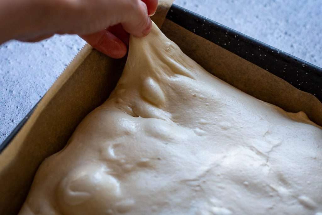 Stretching a corner of focaccia dough to fill all the tray corners.