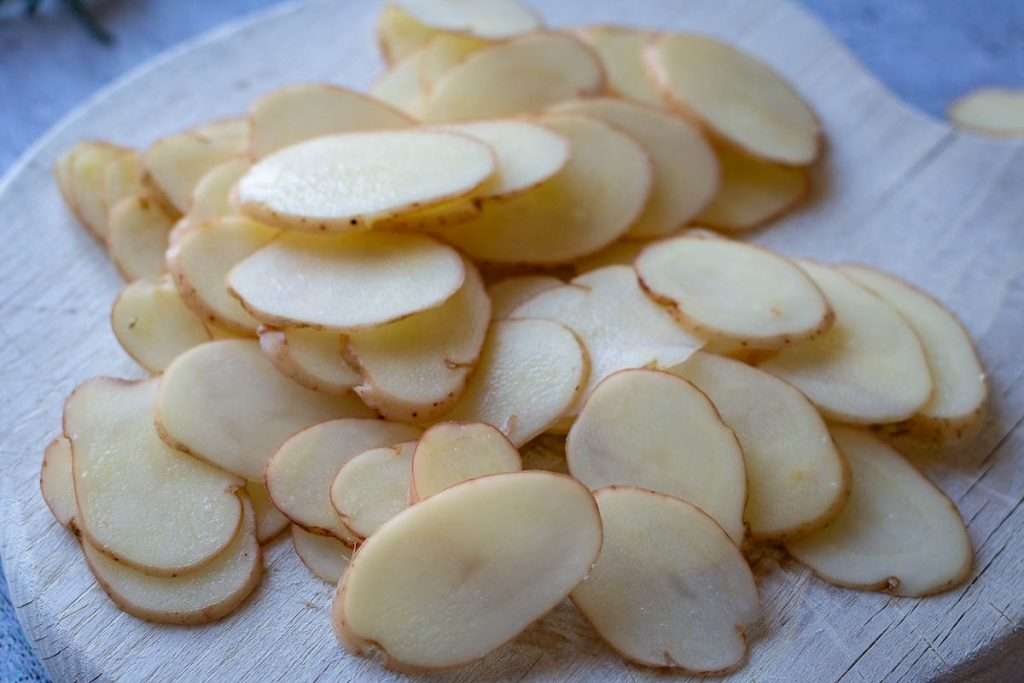 Thinly Sliced waxy potatoes on a wooden chopping board.