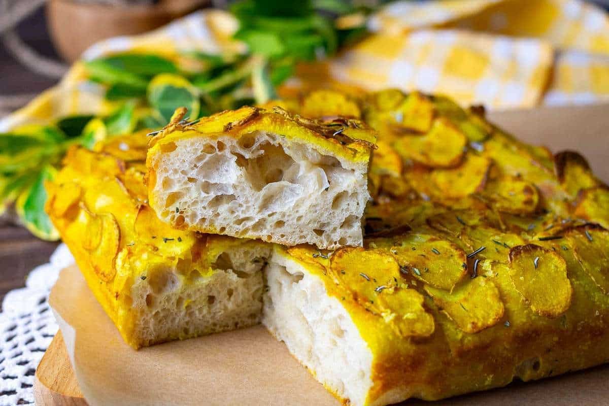 One piece of sourdough focaccia with turmeric potato topping on top of the rest of the focaccia.