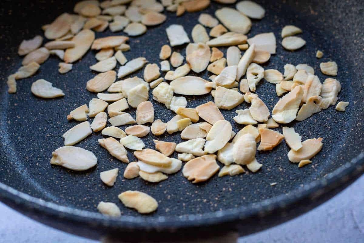 Flaked almonds toasting in a small dry pan.