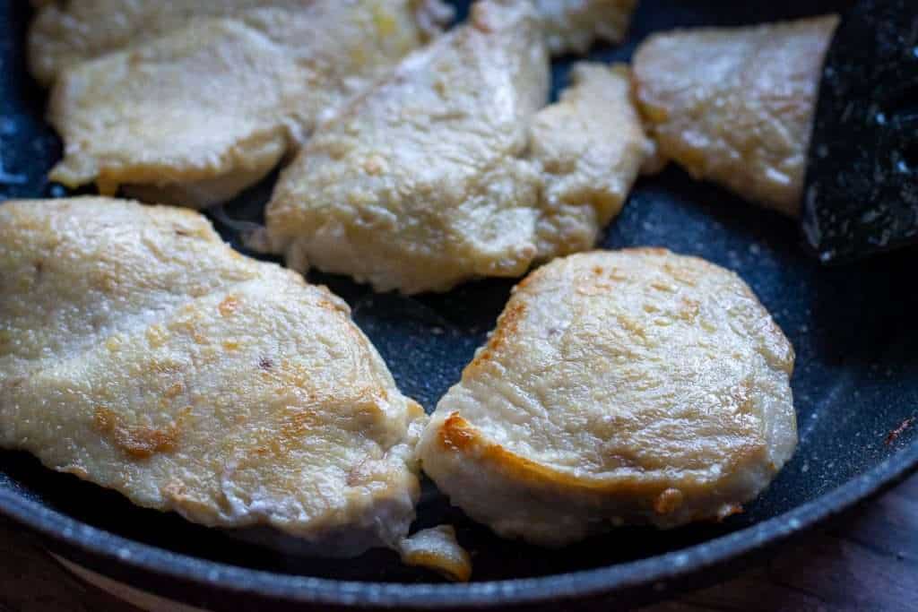 Chicken pieces frying in olive oil in a frying pan.
