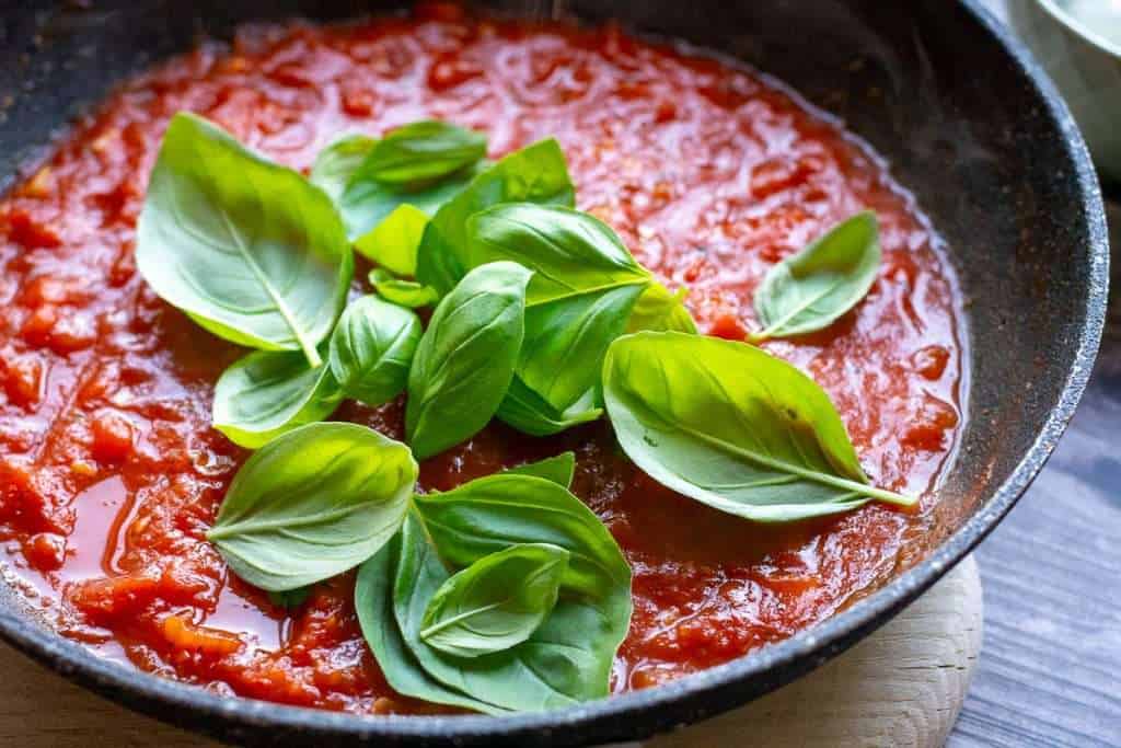 Fresh basil leaves added to the reduced tomato sauce.