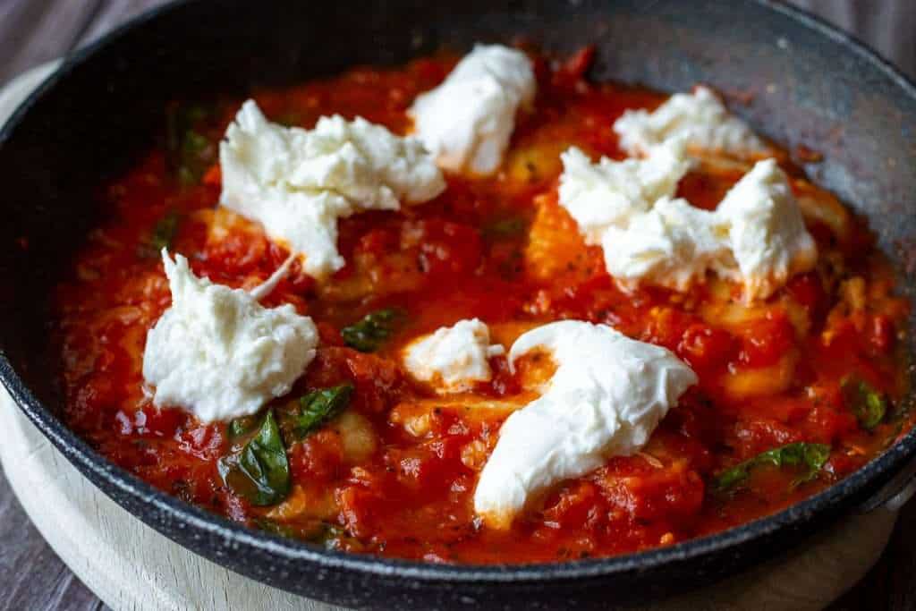 Chicken covered in tomato sauce with torn-up mozzarella on top.