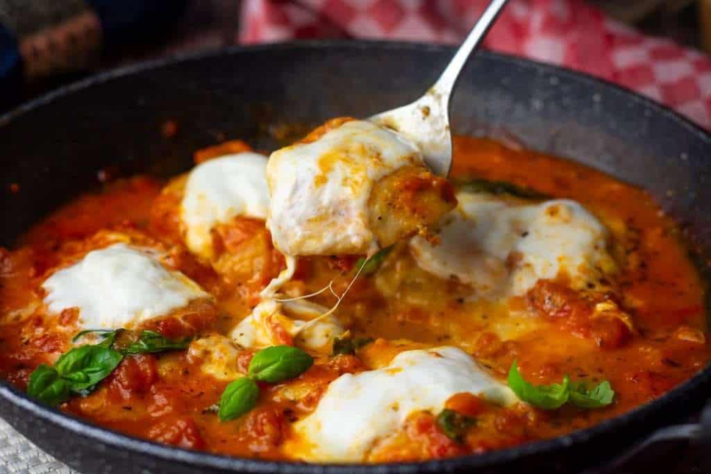 A piece of chicken pizzaiola with melty stringy mozzarella on top being lifted out of the pan with a spoon.
