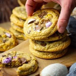 Easter cookies with mini eggs in a few stacks with one cookie being taken.