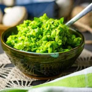Minted Mushy peas in a dark green bowl with a spoon in it.