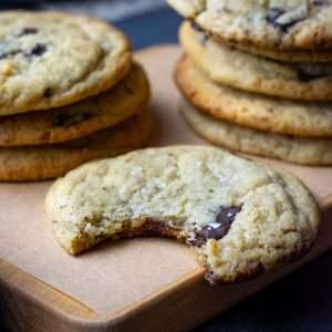 A bitten-into sourdough tahini cookie on a board next to stacks of the cookies.