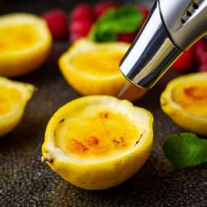 Blow torch heating the top of lemon posset brulee to create caramel topping.