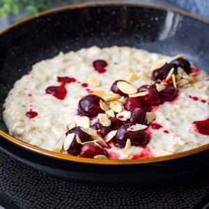 Cherry Bakewell Porridge in a black bowl.