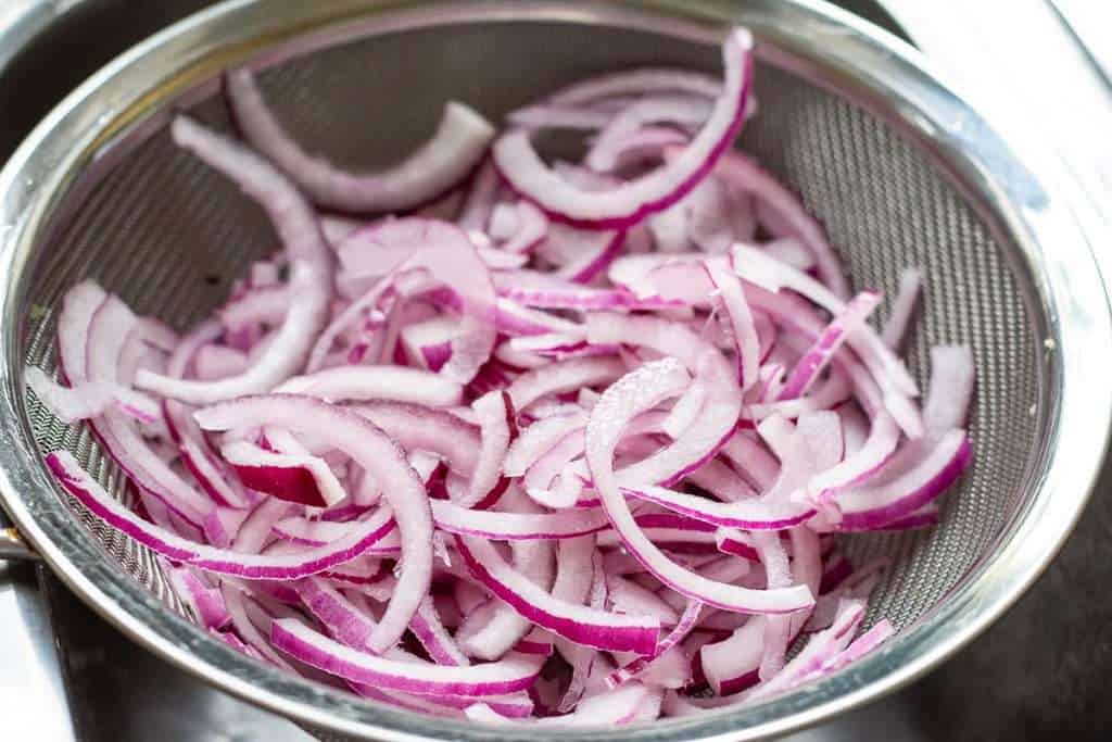 Sliced red onion in a sieve ready to pouring boiling eater over them.