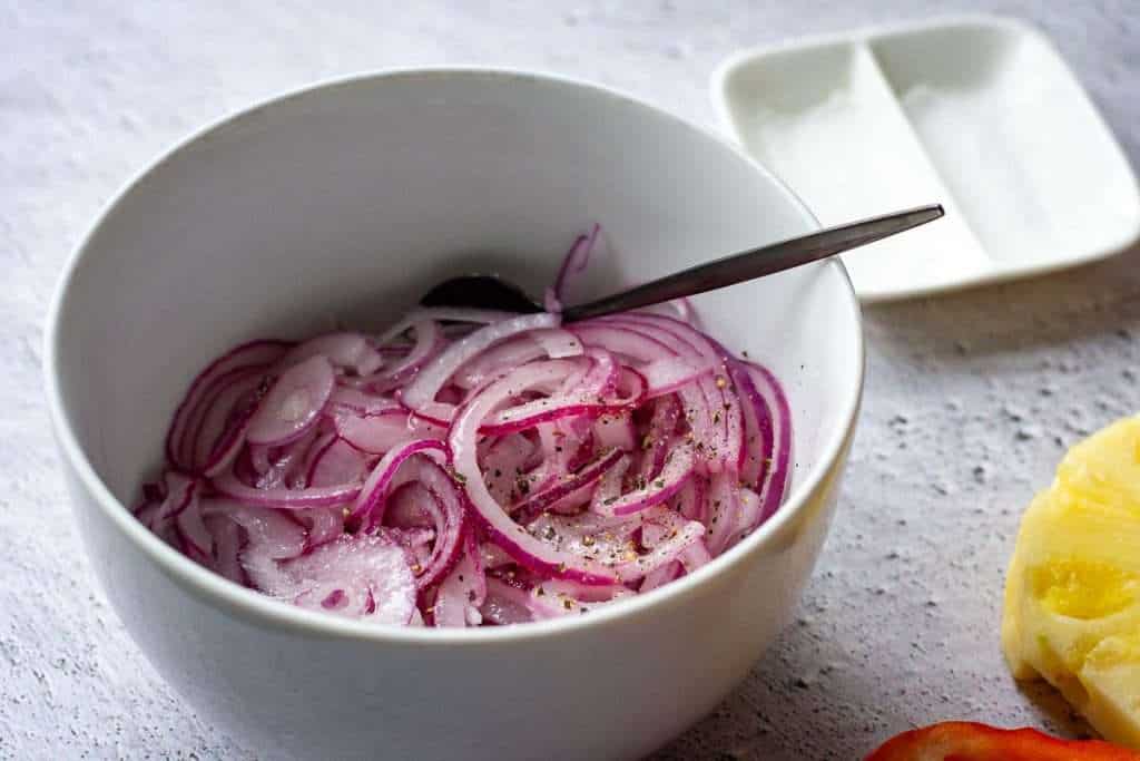 Red onions in a white bowl with pickling liquid.