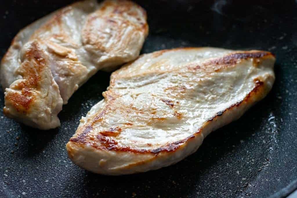 Chicken Breasts searing in a frying pan.