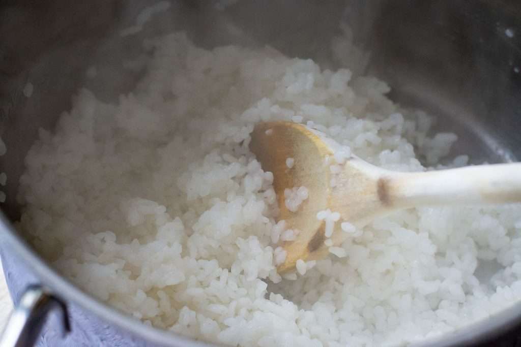 Cooked sushi rice beinf stirred with a wooden spoon.