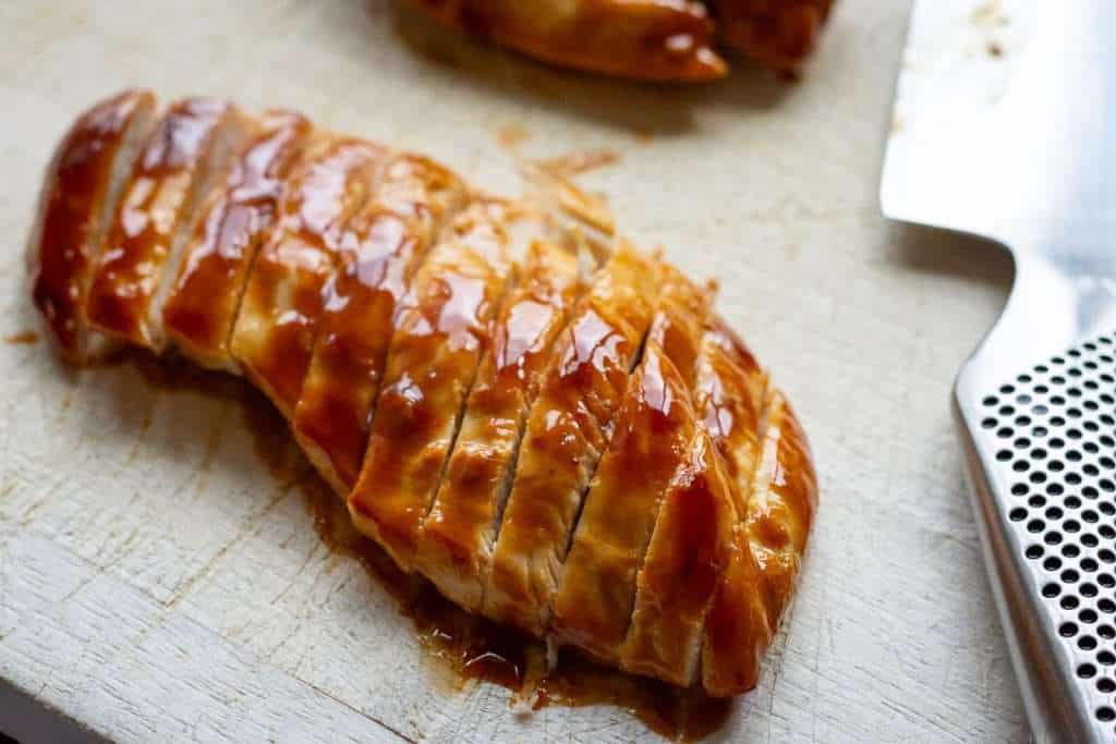 Chicken breast on a wooden chopping board cut into thin strips.
