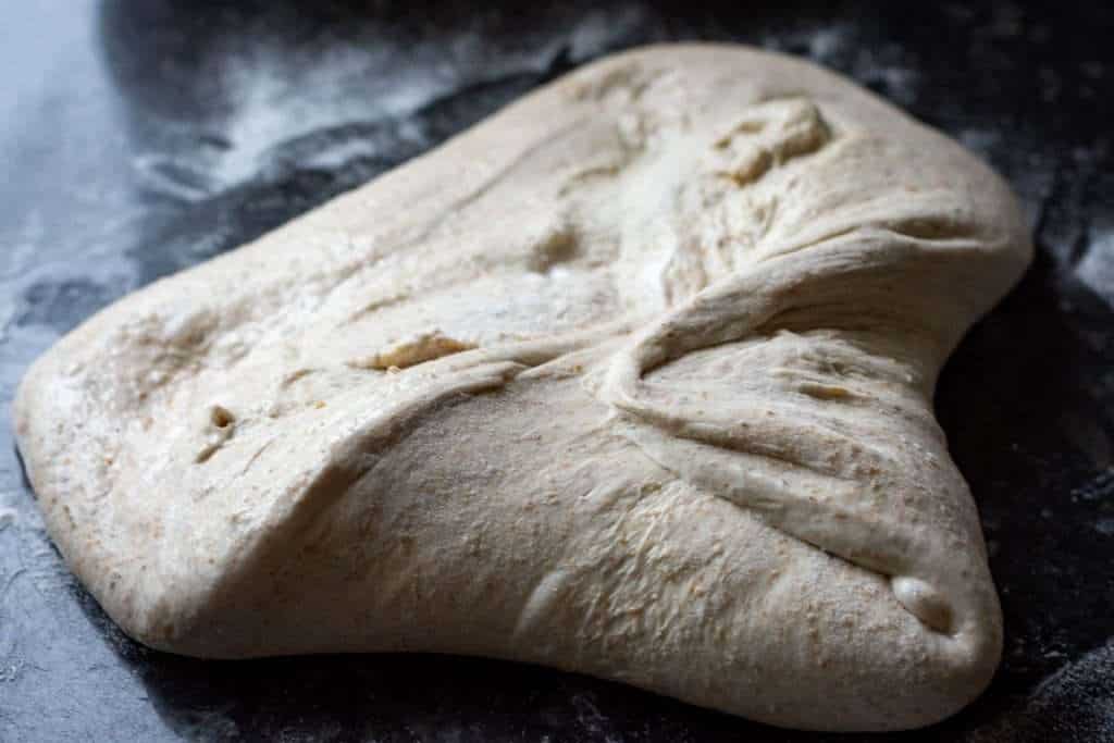 Shaping the ball of sourdough by folding the corners into the centre of the dough.