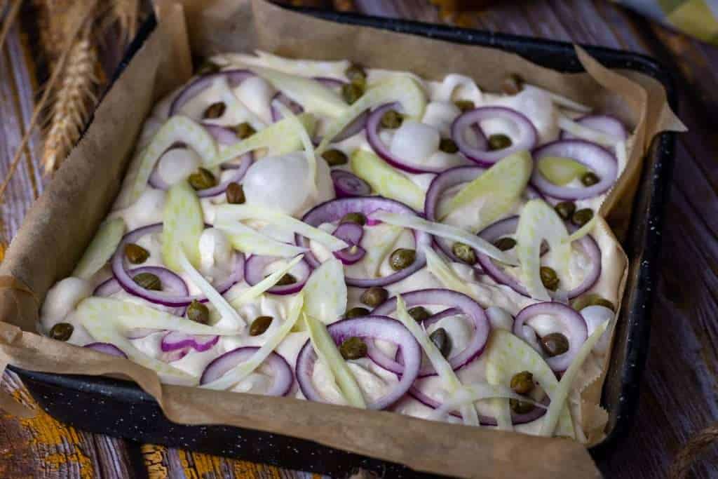 Fennel, red onion and capers arranged on the surface of the sourdough focaccia after its second rise.