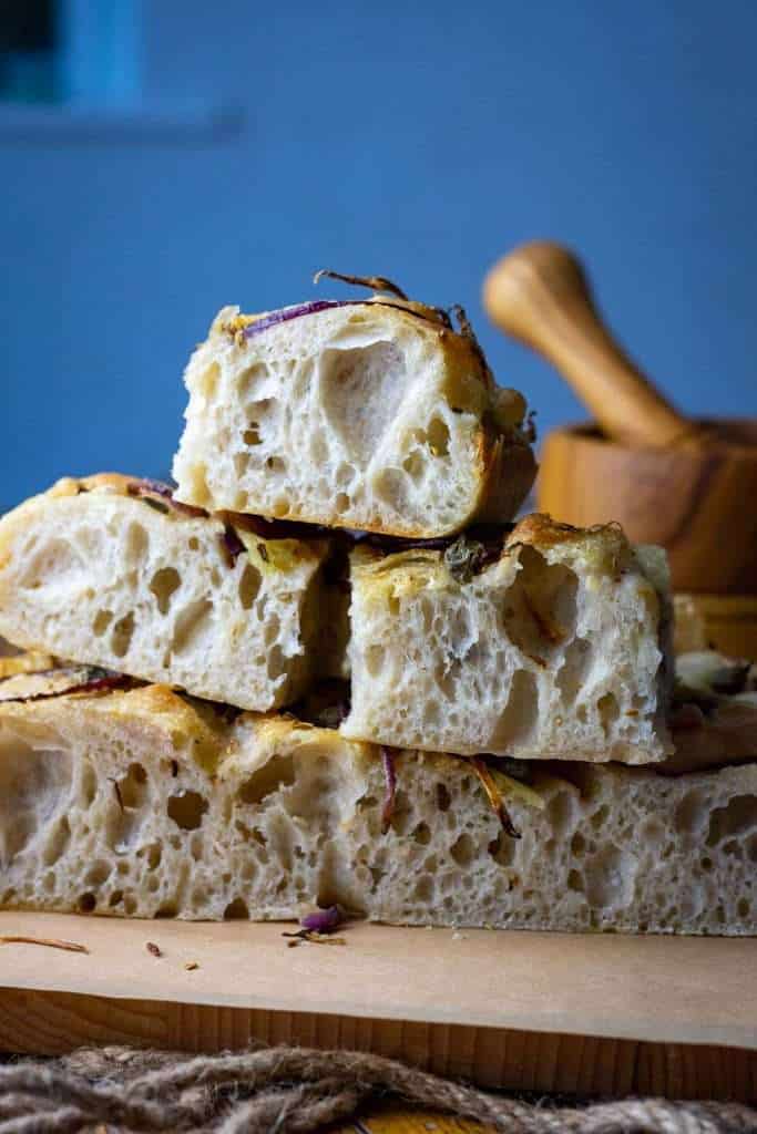 Sliced and stacked sourdough focaccia with fennel and capers on a wooden board.