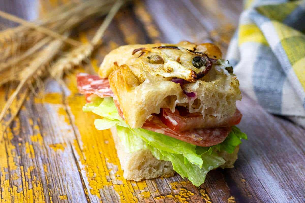 A piece of fennel sourdough focaccia sliced crosswise and stuffed with salami and salad vegetables.
