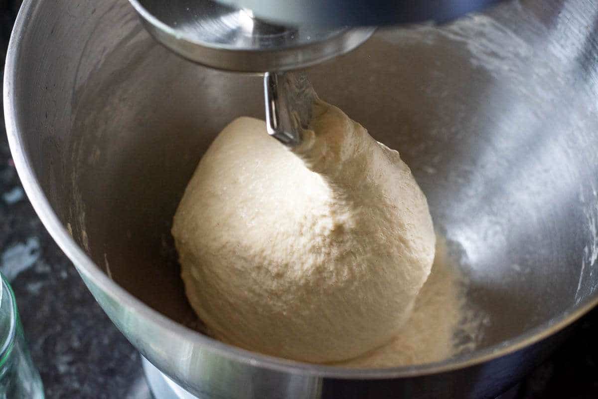 Sourdough focaccia dough gathering around the dough hook attchmen in a bowl of a stand mixer.