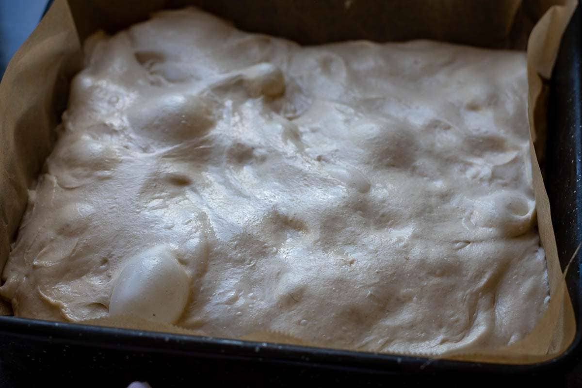 Focaccia sourdough transferred into a parchment paper lined baking tray with high rims.