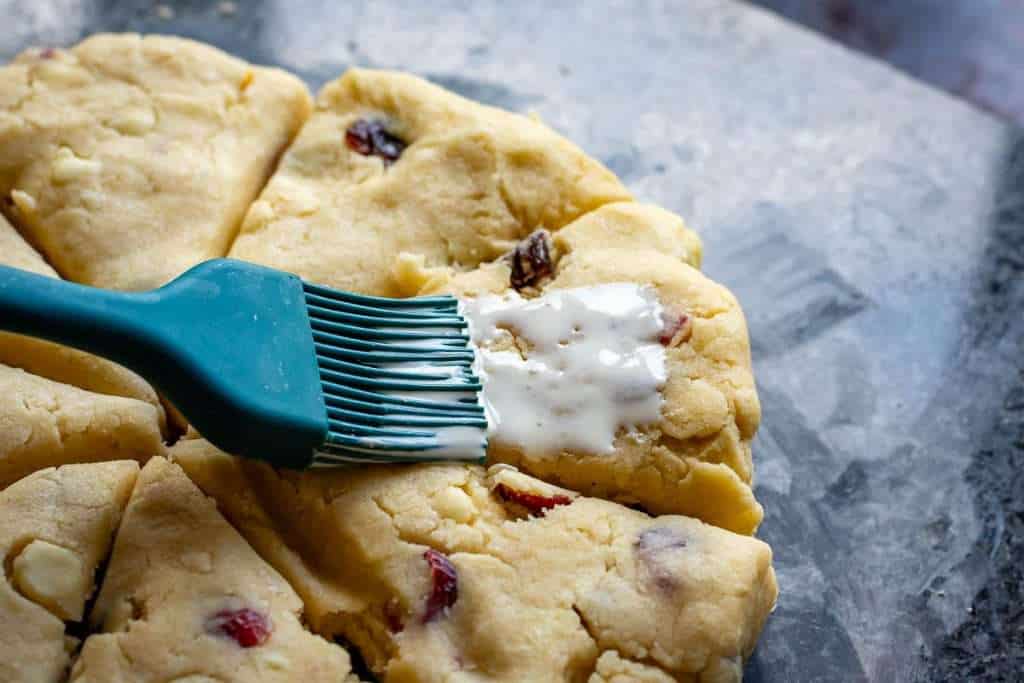Brushing cherry scones with a little milk using a pastry brush.