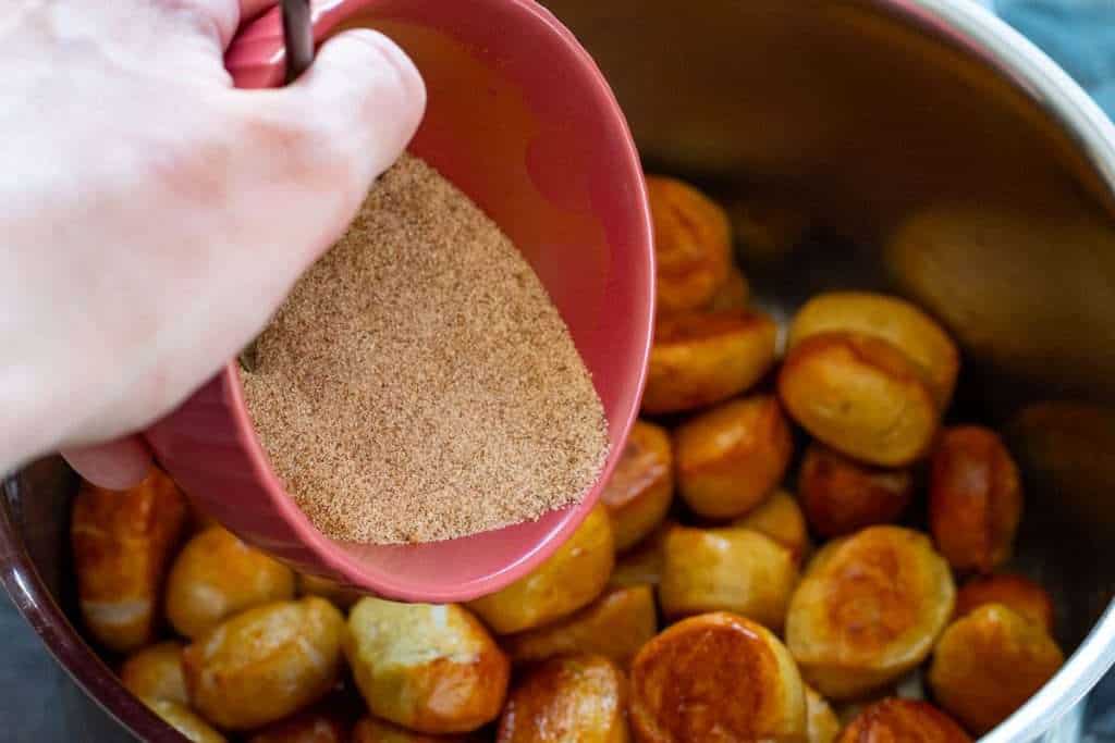 Sprinkling cinnamon sugar over sourdough pretzel bites.