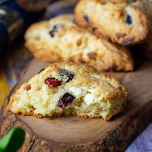 White Chocolate Cherry Scones on a decorative wooden board, one of the scones is broken in half exposing white chocolate chips and dried cherries inside.