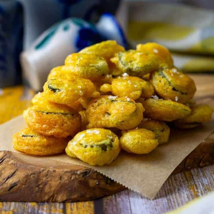 Fried pickles in sourdough discard batter stacked on a small decorative wooden board.