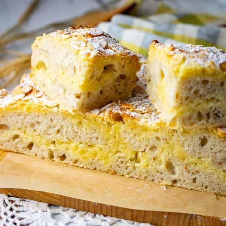 Almond Croissant Sourdough Focaccia cut into squares on a wooden chopping board.