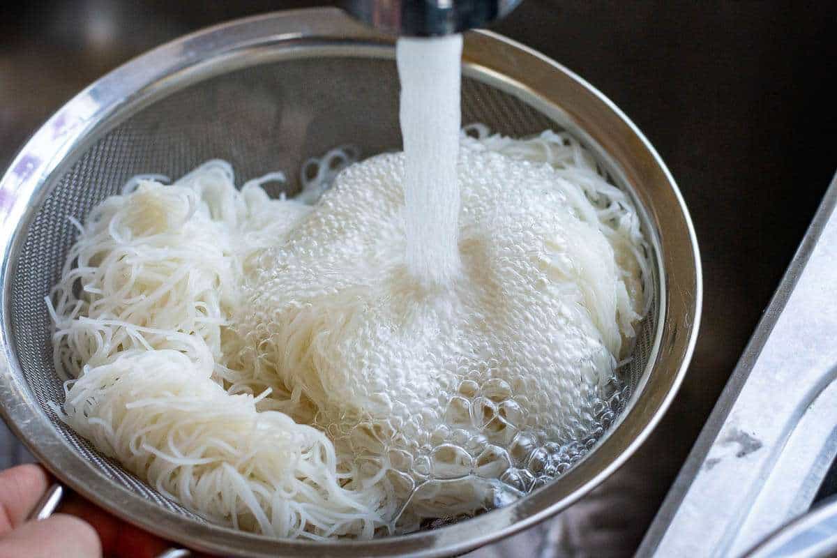 Fine rice noodles in a colander under cold running water.