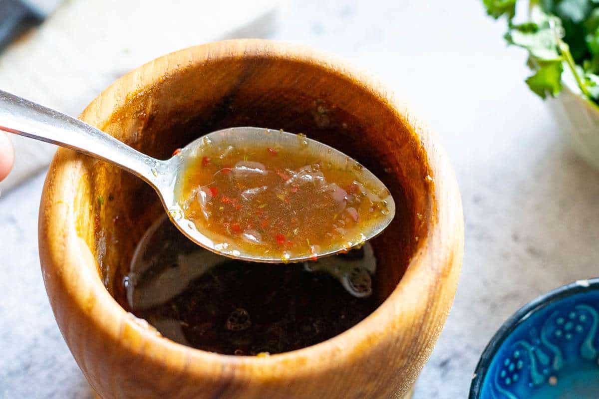 Thai salad dressing in a wooden pestle and mortar with with a spoonful of it lifted out.