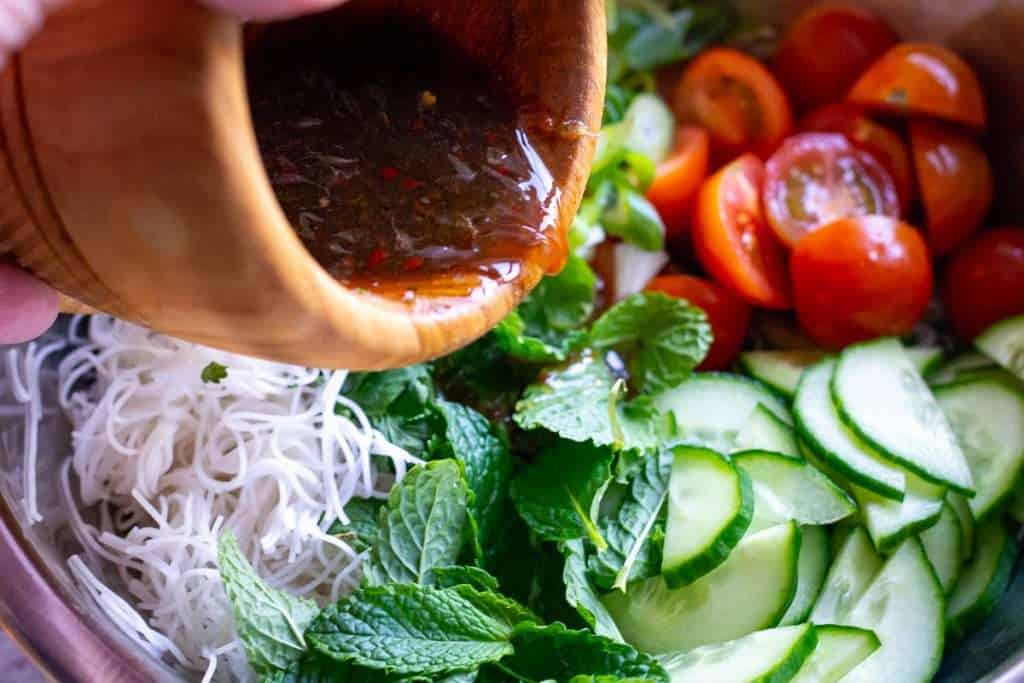 Pouring thai salad dressing over the noodles and vegetables.