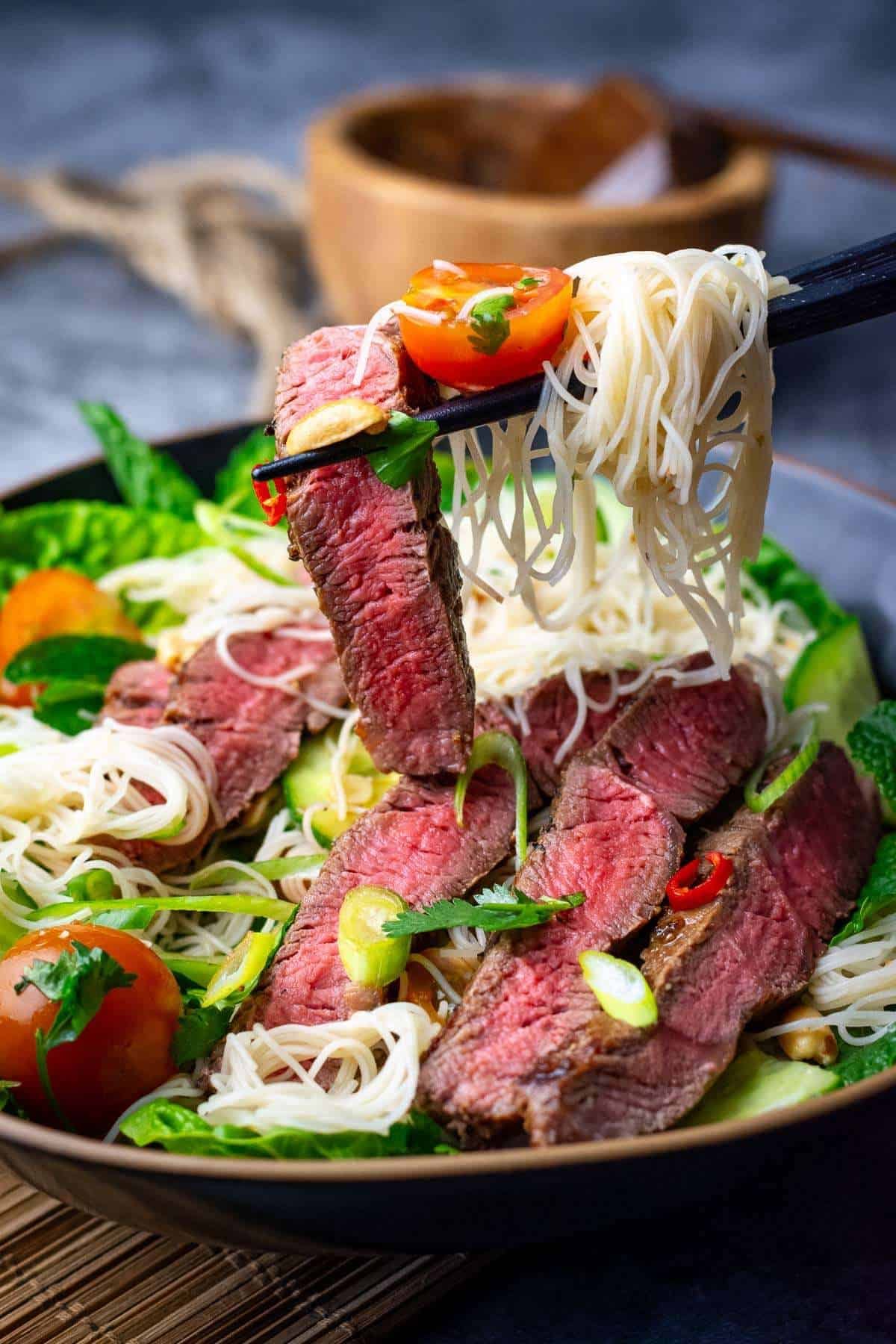 Thai Beef Noodle Salad being picked up by chopsticks from a black bowl.