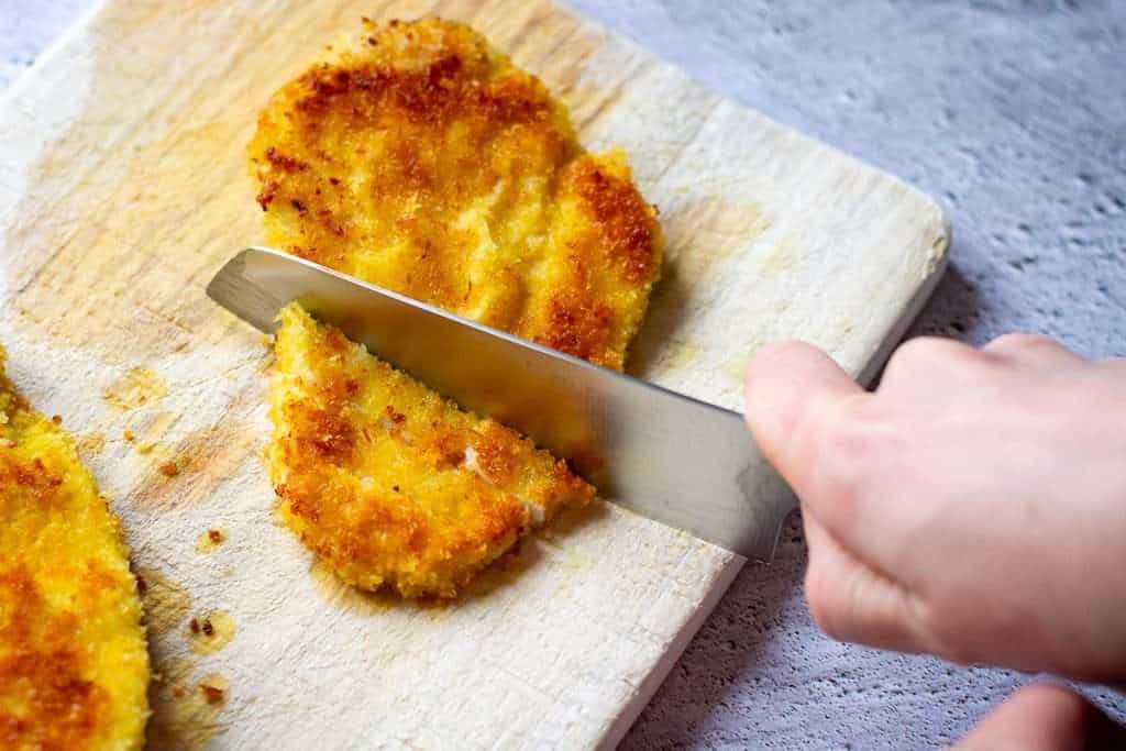 Cutting panko breaded chicken breast pieces into strips.