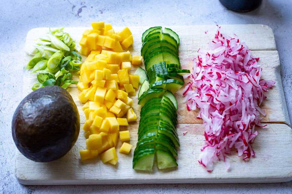 Veggies and mango sliced, chopped and grated on a wooden chopping board.