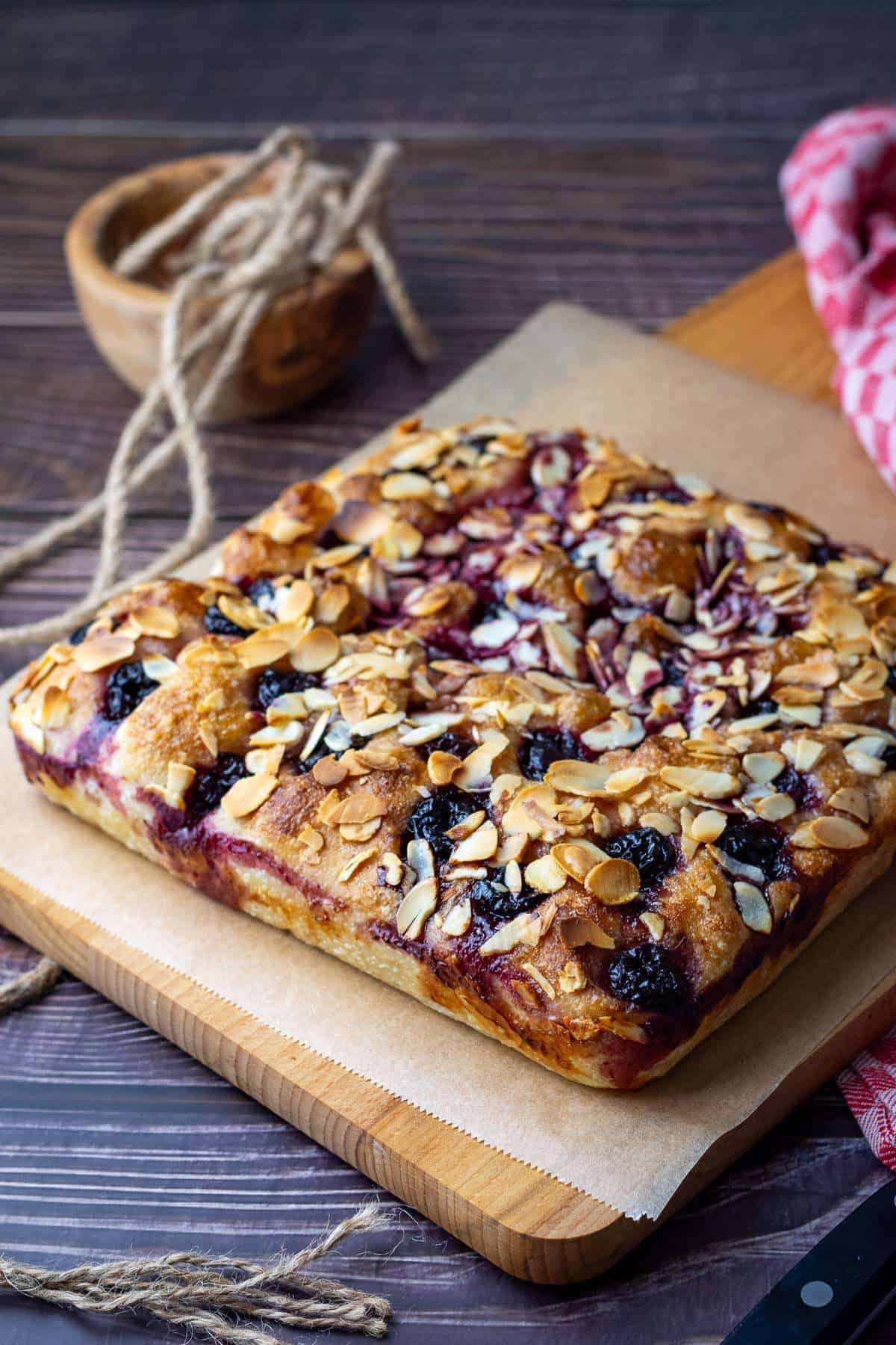 Baked Sourdough Cherry and Almond Focaccia on a wooden board.