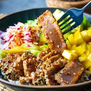 Seared ahi tuna being picked up form a tuna poke bowl.