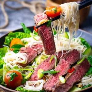 Thai Beef Noodle Salad being picked up by chopsticks from a black bowl.