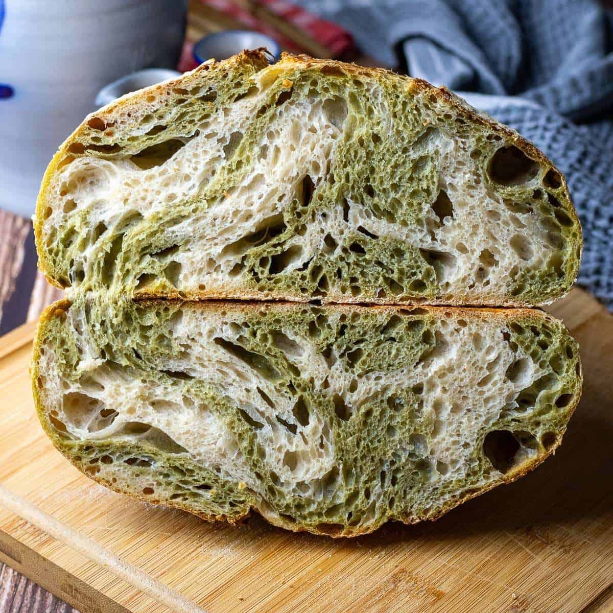 Matcha Sourdough Bread cut in half exposing the matcha swirl on a wooden board.