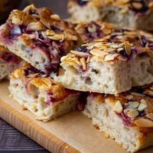 Sourdough Cherry And Almond Focaccia sliced into squaes on a wooden board.