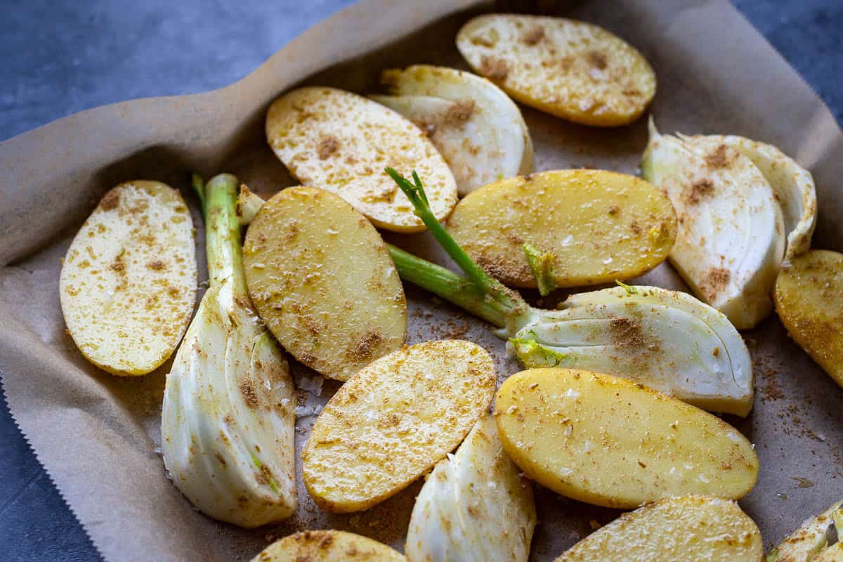 Fennel and halved baby potatoes covered in spices on a baking tray in a single layer.