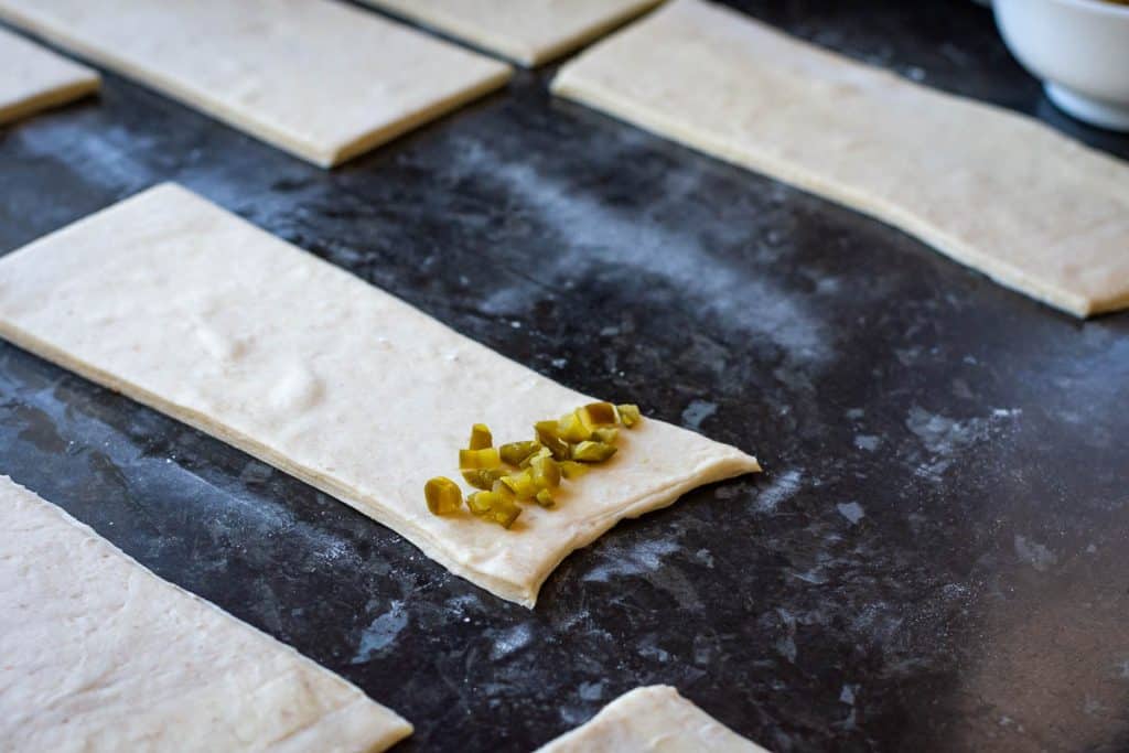 Chopped jalapenos scaterred on the rectangular shaped piece of laminated pastry.