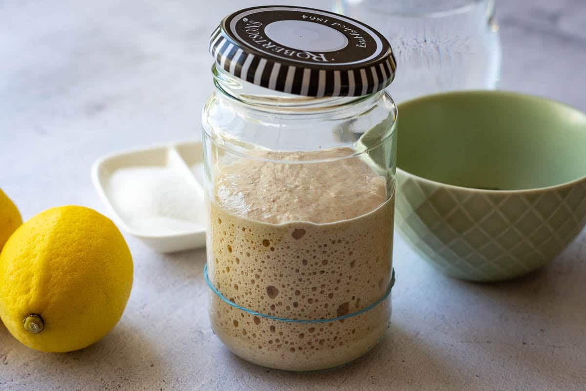 Active sourdough starter on a table with lemon with other ingredients for poppy seed and lemon sourdough.