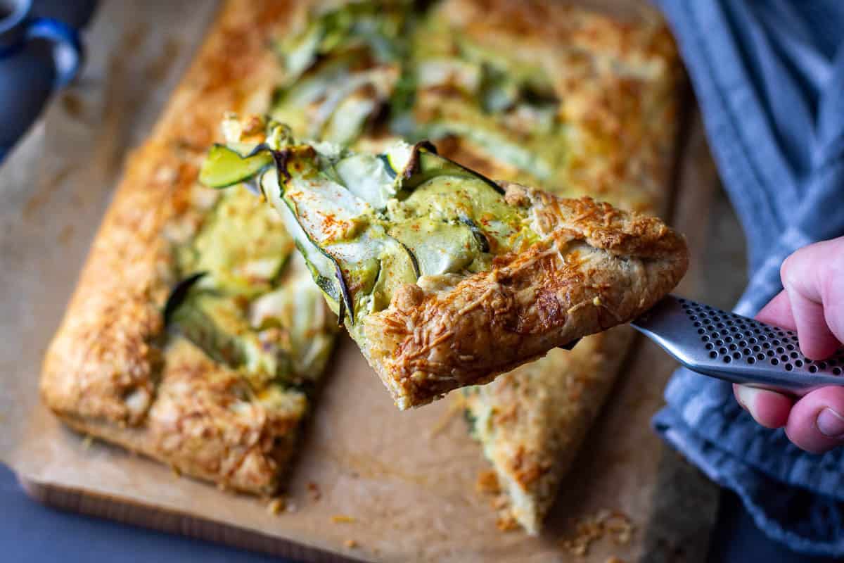A slice of sourdough galette with courgette ribbons and whipped feta being cut.