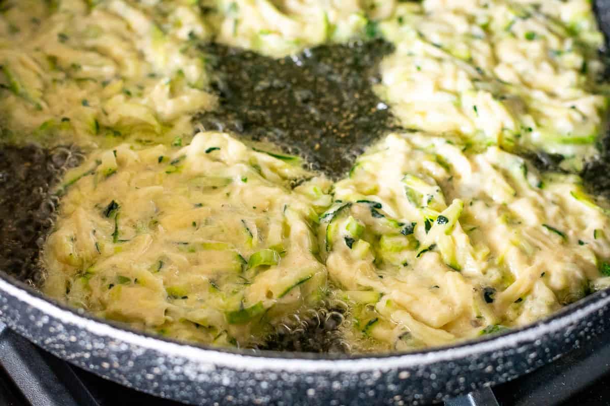 Courgette fritters frying in a pan.