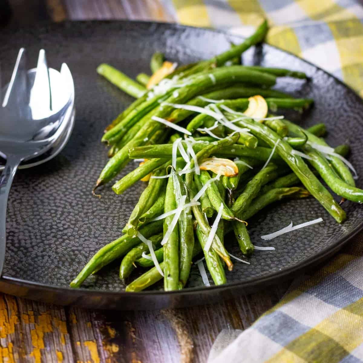 Roasted green beans with garlic, almonds and parmesan on a black plate.