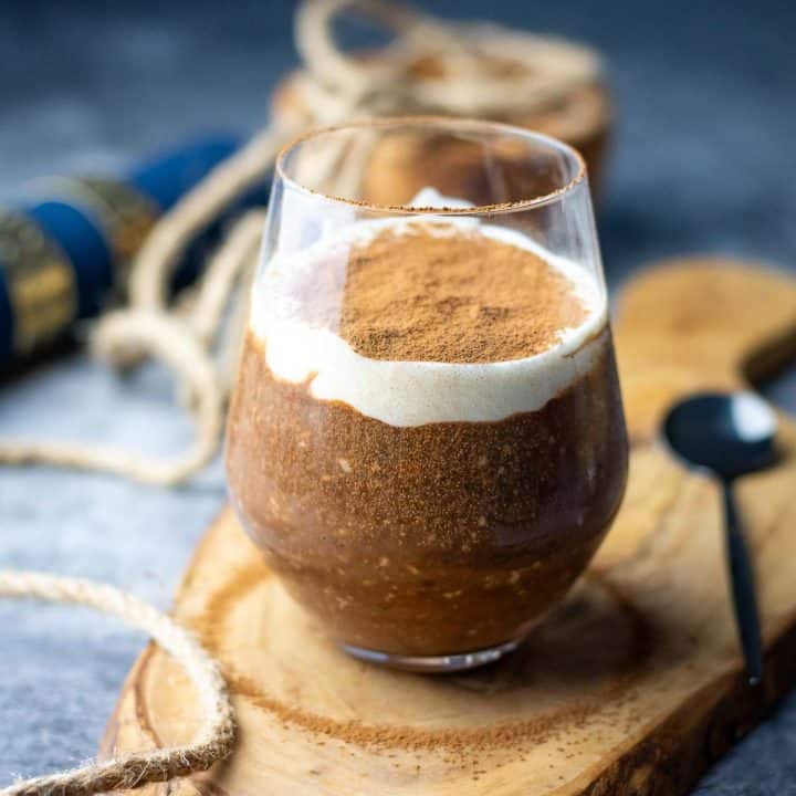 A glass full of tiramisu overnight oats set on a decorative wooden board.