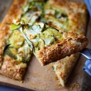 A slice of sourdough galette with courgette ribbons and whipped feta being cut.
