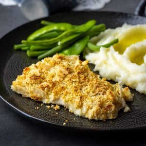 Almond crusted fish on a black plate with mashed potato and green beans.